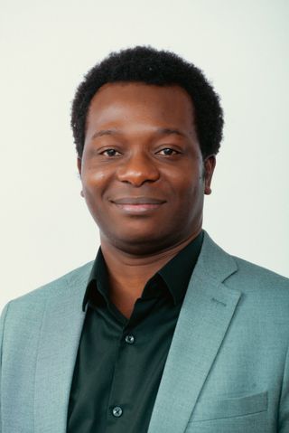Head and shoulders portrait of Dapo Bankole in a sage-green blazer and black shirt, smiling.