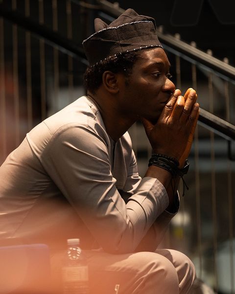 Dapo Bankole seated in profile, hands pressed together at his lips, deep in thought.